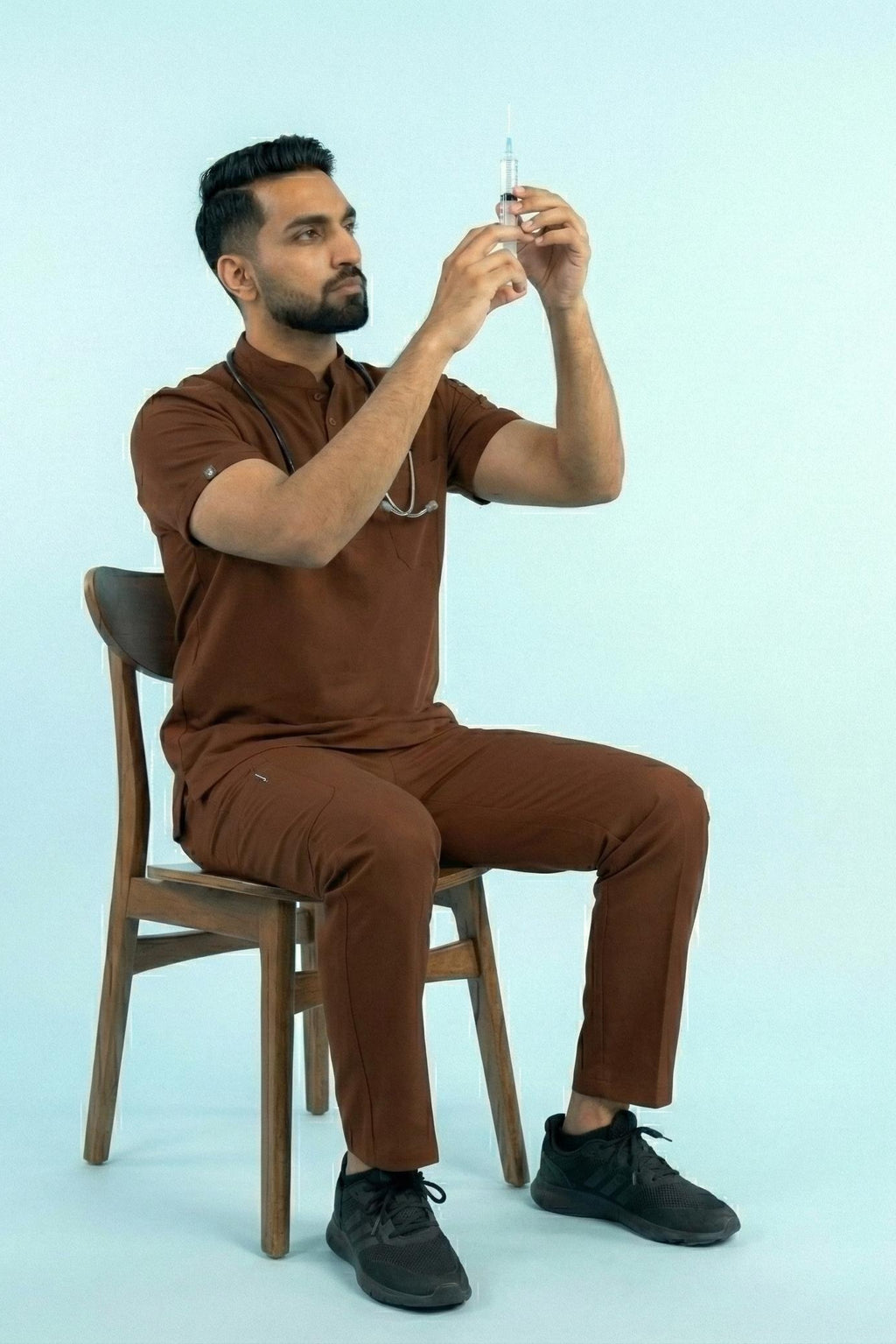 Man in brown outfit sitting on a chair holding a small object against a light blue background
