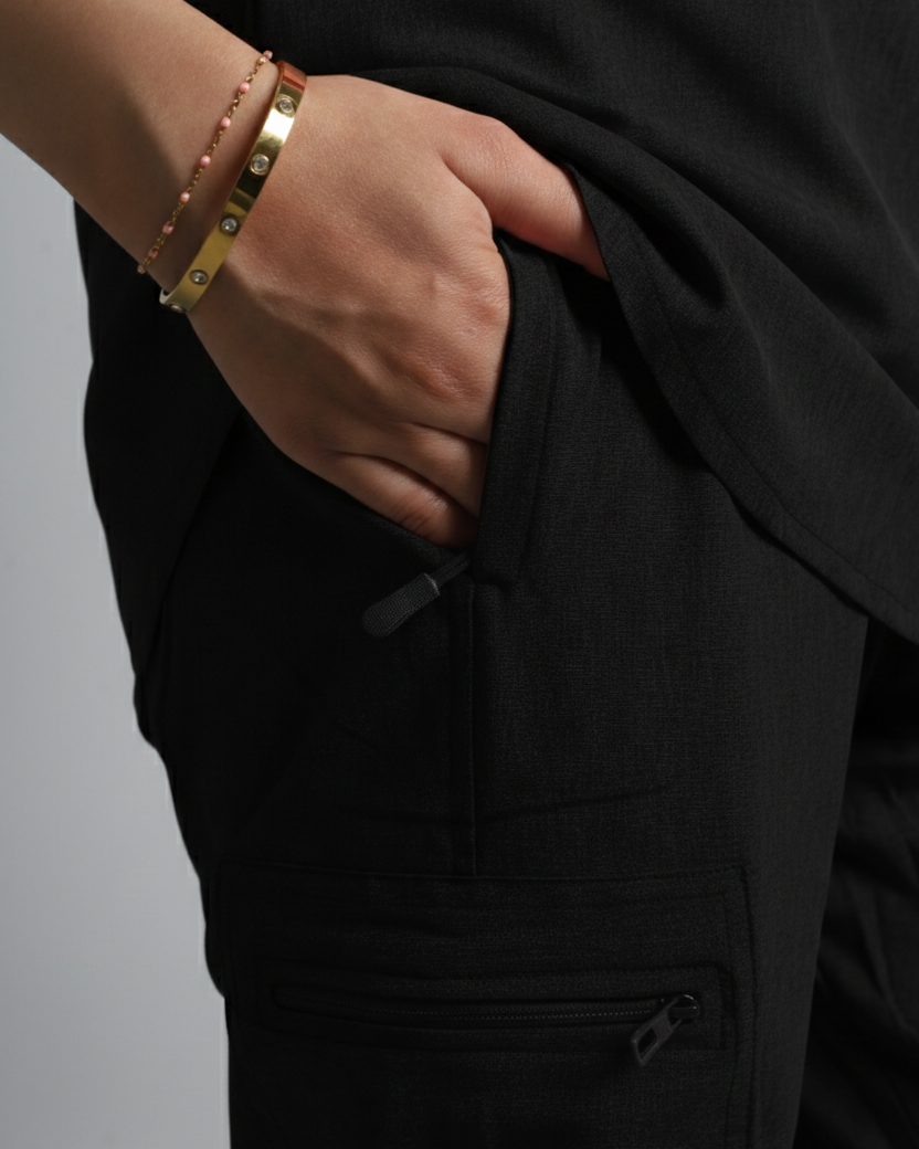 Person wearing a black outfit with gold bracelets on a gray background