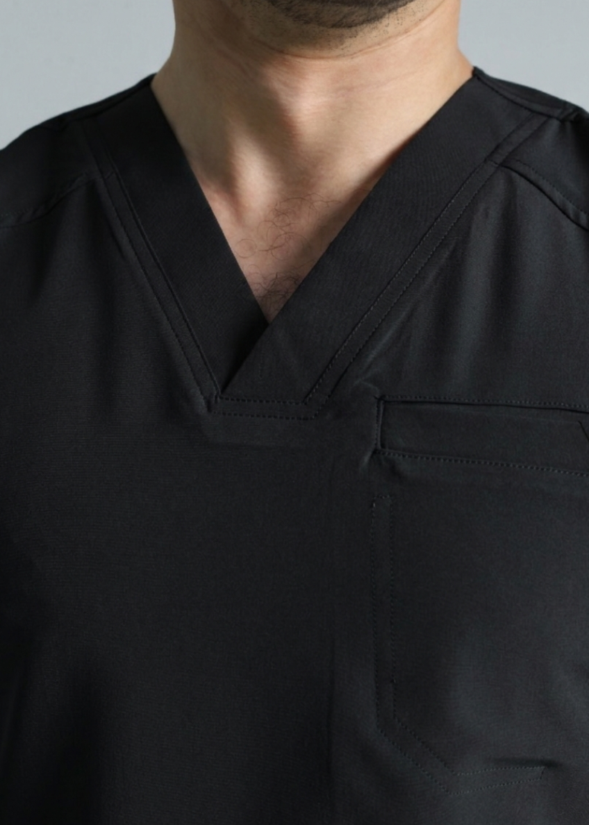 Black scrub top worn by a person against a neutral background