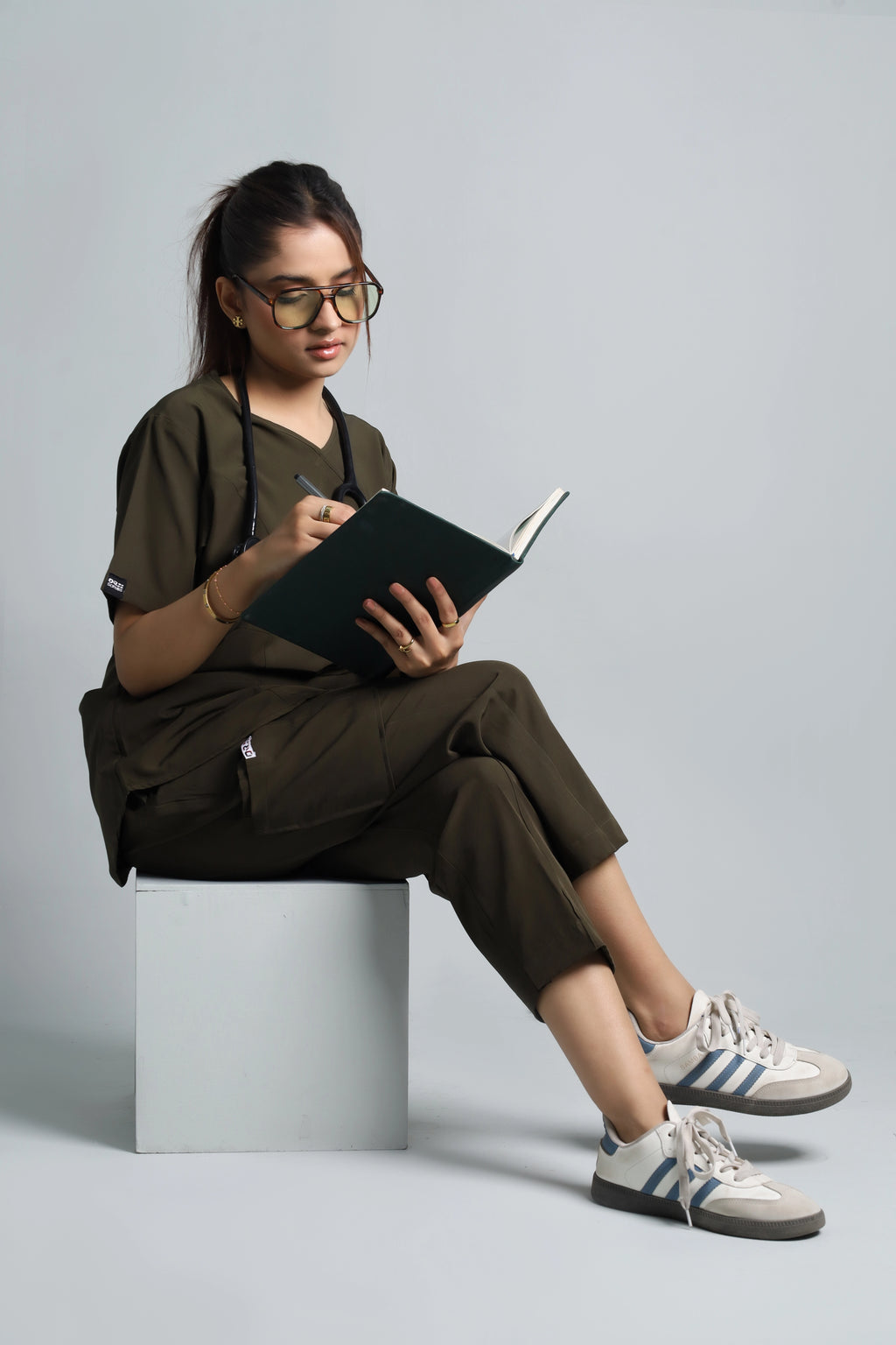 Person sitting on a stool reading a book against a plain background