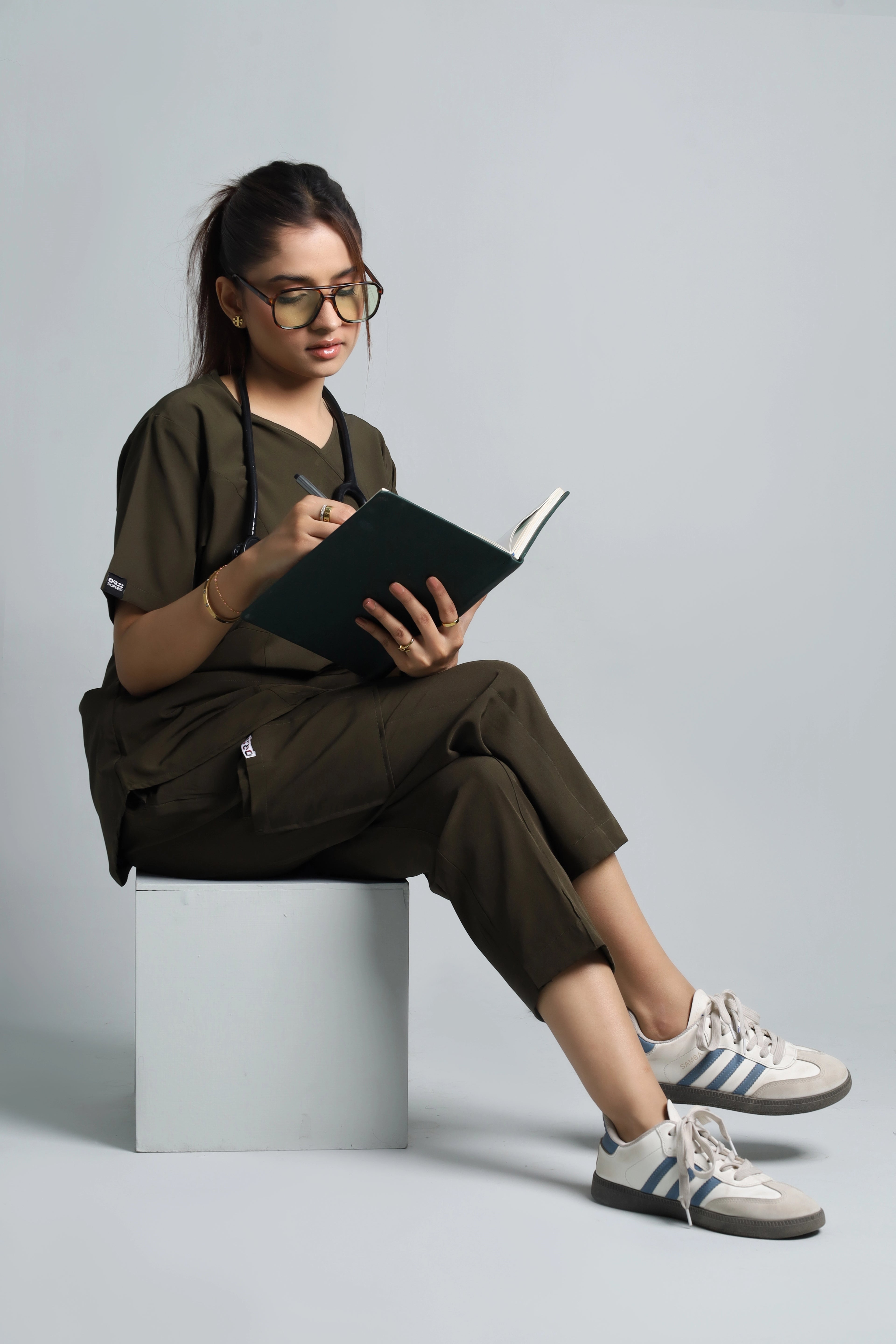 Person sitting on a stool reading a book against a plain background