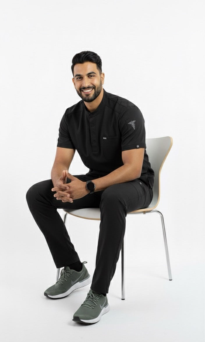 Man sitting on a chair wearing black athletic style medical scrubs with a white background