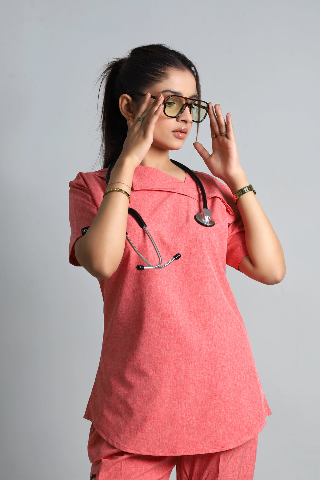 Person wearing a pink medical scrub set with a stethoscope on a gray background
