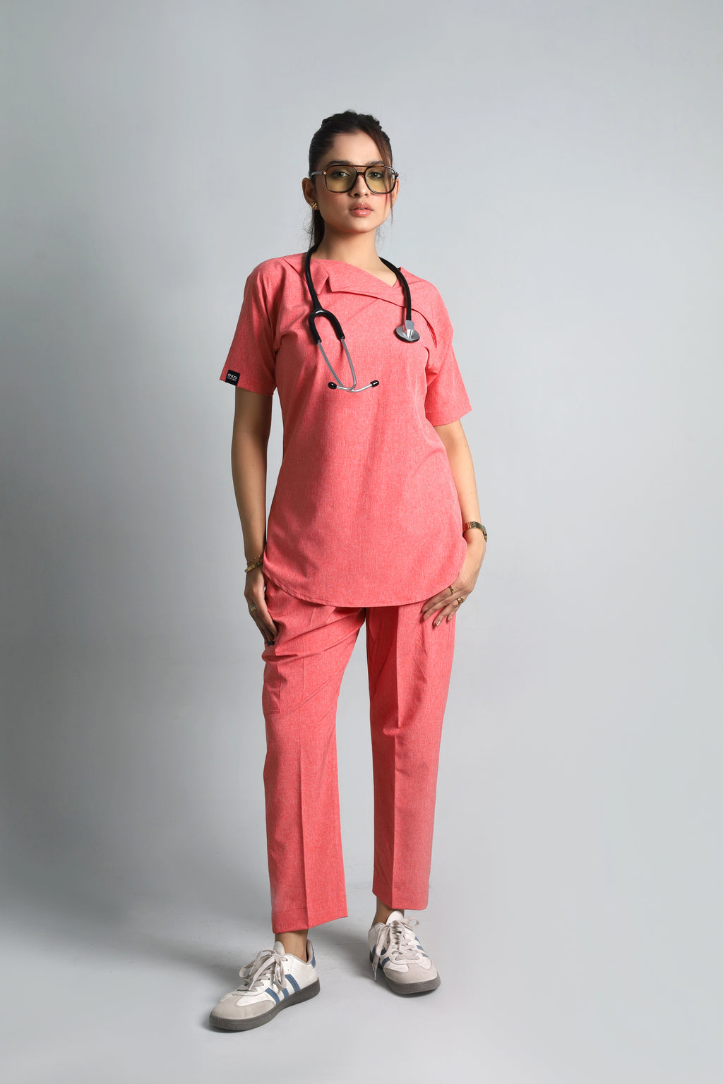 Person wearing a pink medical scrub set with a stethoscope on a gray background