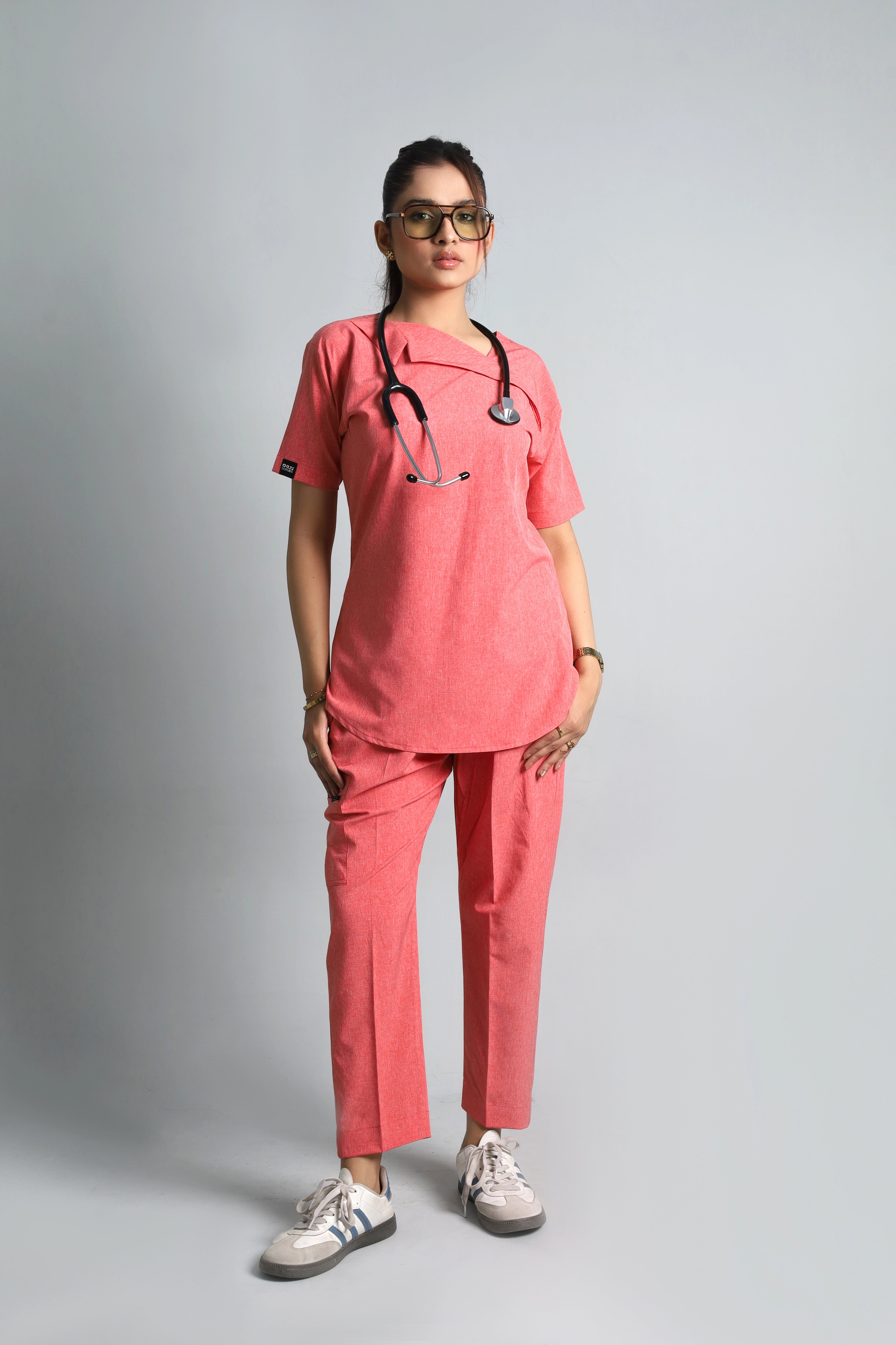 Person wearing a pink medical scrub set with a stethoscope on a gray background